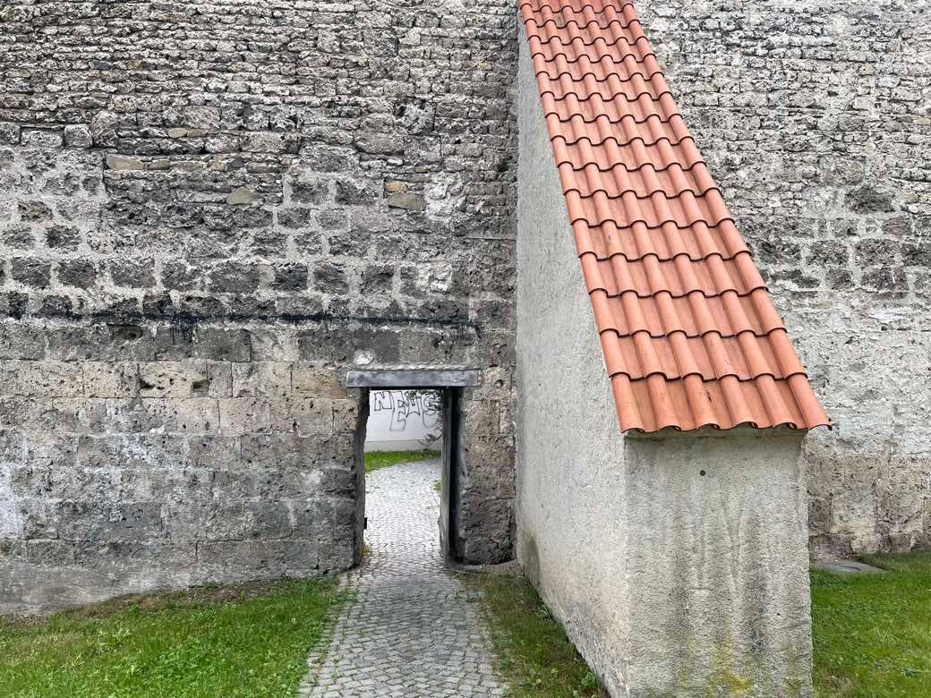 A low doorway through a stone castle wall, a gravel path leading out